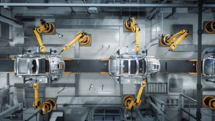 An overhead, bird's-eye view of a modern automotive assembly line. Several yellow industrial robotic arms are positioned around the silver frames of two cars on a conveyor belt, performing precision tasks like welding or assembly in a clean, highly automated factory environment.